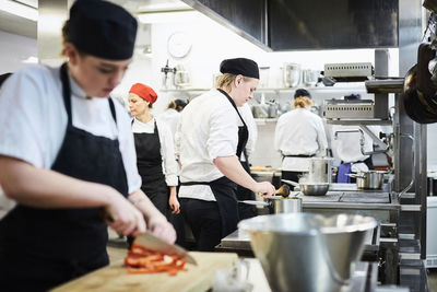 Mature teacher with chef students cooking in commercial kitchen