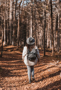 Rear view of girl wearing backpack, hiking in forest in autumn