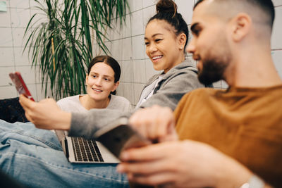 Smiling young businesswoman sharing mobile phone with colleagues while sitting at creative office