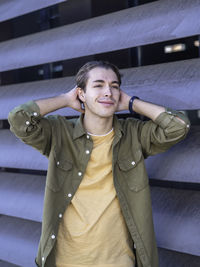 Young positive man in yellow t-shirt and green jacket fixing hair