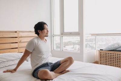 Side view of man sitting on bed