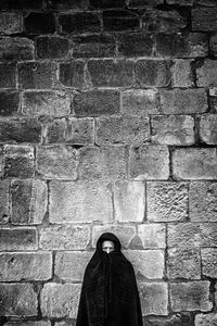 Portrait of woman covered with coat against stone wall