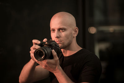 Portrait of young man photographing against black background