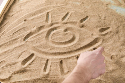 Cropped hand of man drawing on sand 