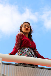 Low angle portrait of woman standing at railing against sky