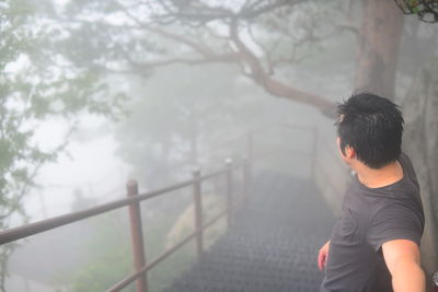 Man standing on steps in forest during foggy weather