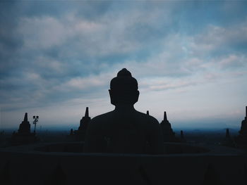 Silhouette buddha statue against cloudy sky during sunset