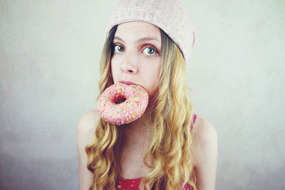 Portrait of young woman eating donut by wall