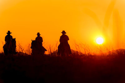 Silhouette people on field during sunset