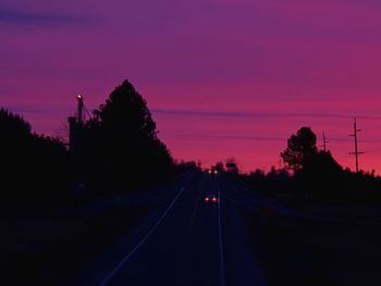 Road by silhouette trees against sky at sunset