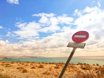 Road sign on beach against sky