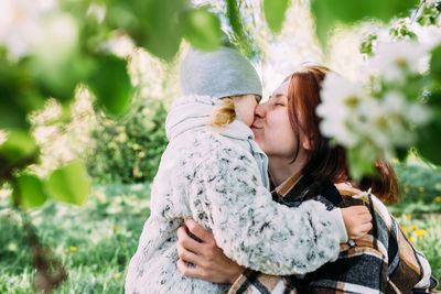 Young woman with her daughter in nature admires white flowering of spring trees