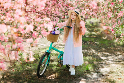 Cute girl with bicycle standing by flowering plant