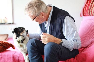 Close-up of man with dog sitting on sofa at home