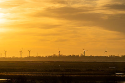 Wind turbines on field against sky during sunset