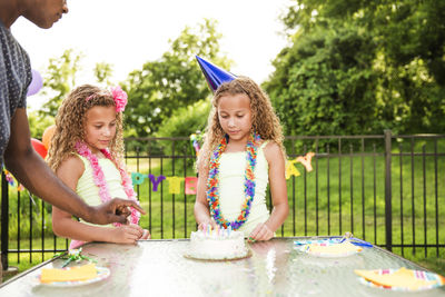 Father standing by girls with birthday cake at table in backyard