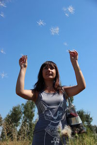 Low angle view of young woman standing against blue sky