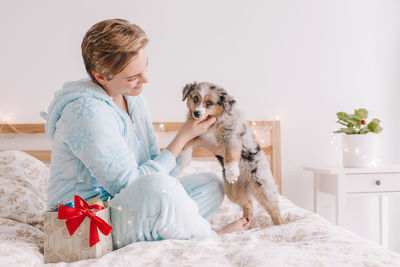 Young woman and dog sitting on bed at home