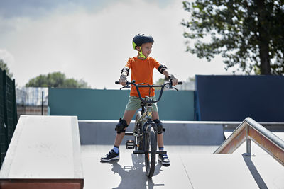 Boy with protective gears sitting on bmx bike at skateboard park