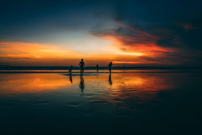 Silhouette people at beach against sky during sunset