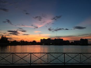 Silhouette buildings by river against sky during sunset