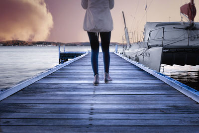 Low section of woman standing on pier against sky during sunset