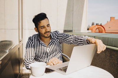 Young man using laptop while sitting in balcony at hotel