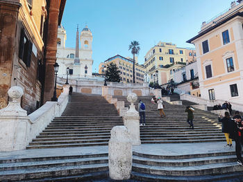 People on staircase amidst buildings in city against sky