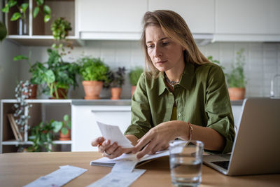 Freelance accountant working at home comparing figures in bills and financial document in laptop