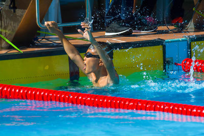 Shirtless boy with arms raised swimming in pool