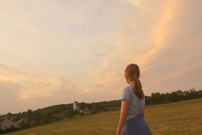 Girl standing on field against sky during sunset