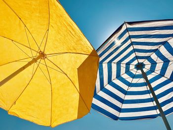 Low angle view of beach umbrellas against clear blue sky