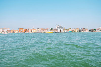 Buildings by sea against clear blue sky