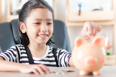 Girl putting coin in piggy bank at home