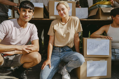 Portrait of smiling male and female volunteers crouching by donation boxes at community center
