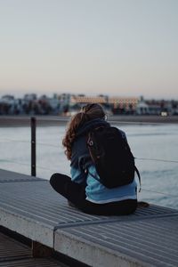 Woman sitting on pier against sky during sunset