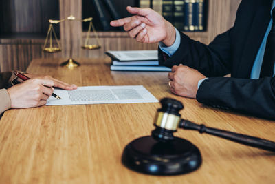 Midsection of judge gesturing while client signing contract on table