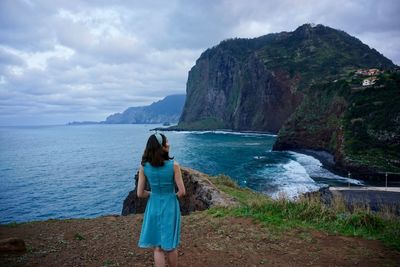 Rear view of woman standing on sea shore against sky