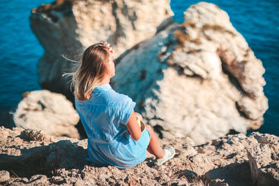 Rear view of woman sitting on rock over sea