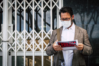 Man wearing face mask holding paper with text against built structure