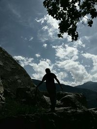 Low angle view of silhouette man standing on rock against sky