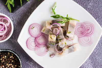 Sliced salted herring with onions and arugula on a plate on the table. simple snack. top view. 