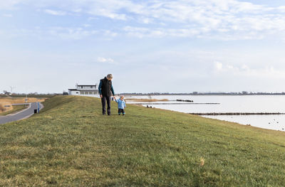 Grandfather holding hands with granddaughter on grassy field against sky