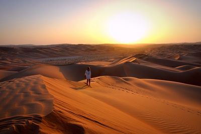 Woman walking on desert against sky during sunset