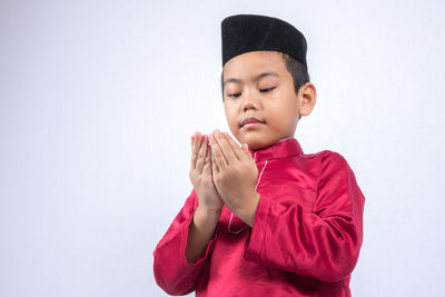 Cute boy wearing maroon traditional clothing standing against white background