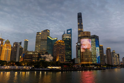 Illuminated buildings by river against sky in city