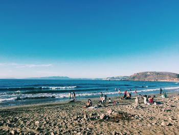 People relaxing on beach against clear blue sky