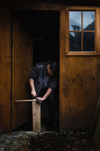 Man working on wood at door of house