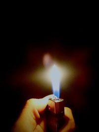 Close-up of hand holding lit candle in dark room