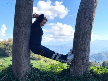 Side view of man sitting on tree trunk